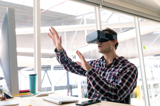 Male graphic designer using virtual reality headset at desk