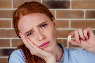 redhaired ginger female with pain grimace holding white wisdom tooth after surgery removal...