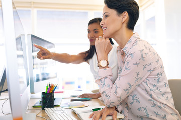 Female graphic designers discussing on computer at desk in a modern office