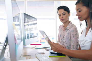 Female graphic designers discussing on digital tablet at desk in a modern office