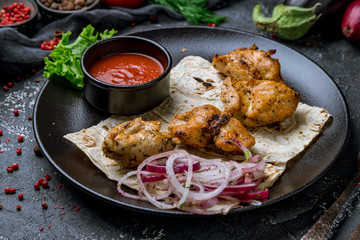 chicken kebab on black plate with tomato sause