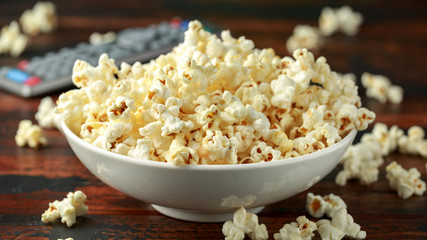 bowl of salty popcorn and remote control on wooden table
