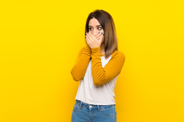 Pretty young woman over isolated yellow wall covering mouth and looking to the side