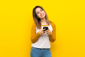 Pretty young woman over isolated yellow wall sending a message with the mobile