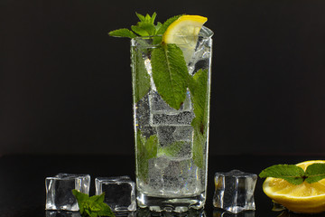 Clear water in glass with green mint leaves and ice cubes on black background