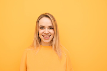 Close-up portrait of a smiling teenage girl on a orange background, wearing a casual clothing, looking into the camera and rejoicing. Positive girl isolated on yellow background.