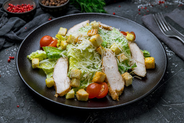 Salad caesar with chicken on black plate