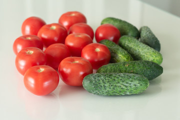Fresh tomatoes and cucumber on a white glass kitchen table. Fresh organic food ingredients. Top view.