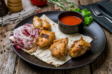 chicken kebab on black plate with tomato sause