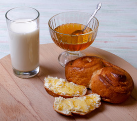 photo Breakfast glass of milk, bun bun, honey in a bowl and sandwiches with cottage cheese poured with honey