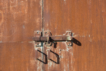 Background of old iron rusty gate. Metal gate with red rust. The texture of a rusty gate with a hinged and padlock lock. Gates with door handles.