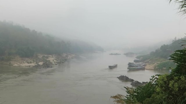 Large muddy river with boats on a very cloudy and thick fog