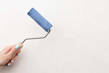 Female hand painting wall with roller in blue color, copy space