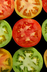 Halves of red, green and yellow tomatoes on black background top view
