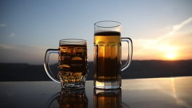 Glass of beer on a beach at sunset. Cooling summer drink concept. Close Up of A Glass of Draught Beer with the Bokeh of Sunlight Background, Soft Focus