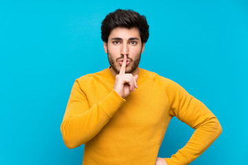 Handsome over isolated blue wall showing a sign of silence gesture putting finger in mouth