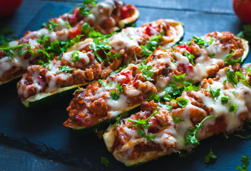 Close-up of stuffed zucchini boats with ground beef, spicy tomato sauce, cheese and fresh parsley, on dark background - Powered by Adobe