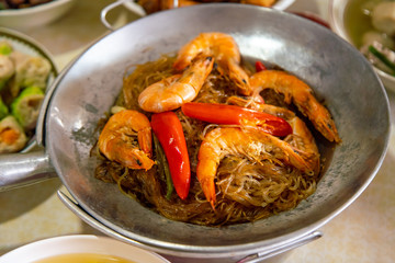 Casseroled prawns with Glass Noodels in Small Iron Pan with Fish, Fried Spring Rolls, Dim Sum, Seafood, Roasted Duck and Meatball Background on the Table.