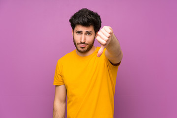Handsome over isolated purple wall showing thumb down with negative expression