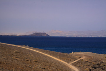 Panoramic view from cliff at Punta del Papagayo (Lanzarote) over blue ocean on Fuerteventura and...