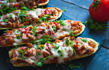 Close-up of stuffed zucchini boats with ground beef, spicy tomato sauce, cheese and fresh parsley, on dark background