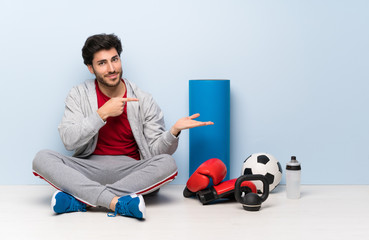 Sport man sitting on the floor holding copyspace imaginary on the palm to insert an ad
