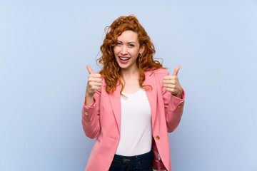 Redhead woman in suit over isolated blue wall with thumbs up gesture and smiling
