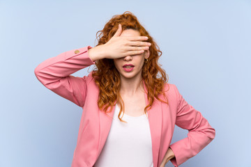 Redhead woman in suit over isolated blue wall covering eyes by hands. Do not want to see something