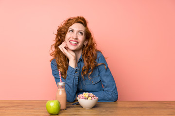 Redhead woman having breakfast cereals and fruit laughing and looking up