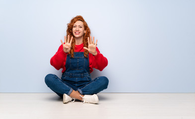 Redhead woman with overalls sitting on the floor counting nine with fingers