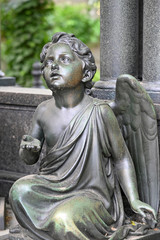 A black sculpture of a little, begging angel on a tomb in Berlin-Germany.