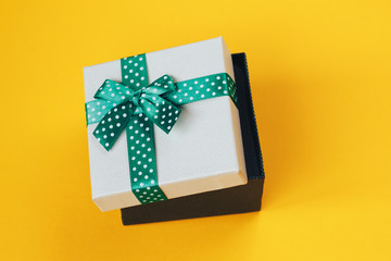 Gift box with green ribbon on yellow background.