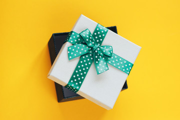 Gift box with green ribbon on yellow background.