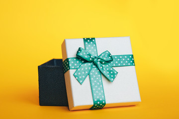 Gift box with green ribbon on yellow background.