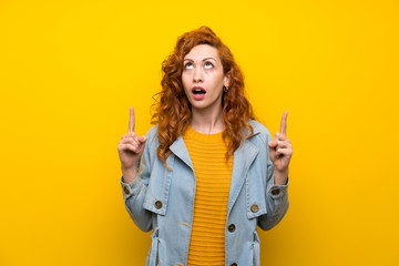 Redhead woman over isolated yellow background pointing with the index finger a great idea