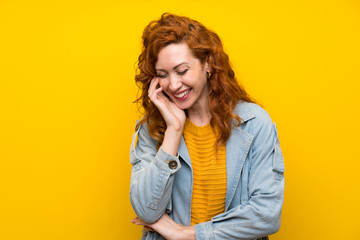 Redhead woman over isolated yellow background laughing