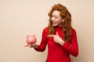 Redhead woman with turtleneck sweater holding a big piggybank