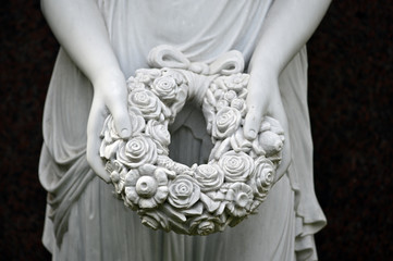 A white sandstone sculpture of an angel with a laurel wreath in her hand. 