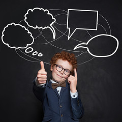 Smart child boy with thumb up and empty speech clouds bubbles on chalkboard