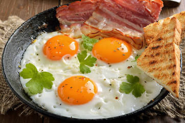 Fried eggs, bacon and toasts on frying pan