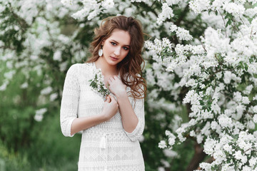 A beautiful young girl stands among the flowering trees. White flowers. Spring. A girl with her...