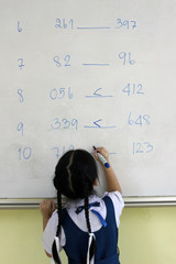 Primary school girl solves greater than or less than math equations on a classroom whiteboard
