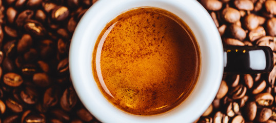 Roasted coffee beans with cup of espresso on dark background