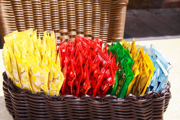 Close up of wooden basket with choice of small colorful plastic packages of sauces on table of...