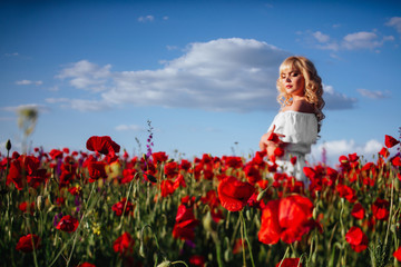 Fototapeta na wymiar cheerful girl with curly blond hair in a huge poppy field alone, springtime, sunset