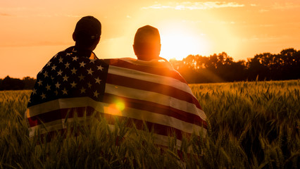 A man and his son admire the sunset over a field of wheat, wrapped in the flag of the USA © StockMediaSeller