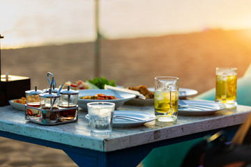 Food and beverage on the table at beach bar for dinning party on the beach and have sunset light and blurry sea background.