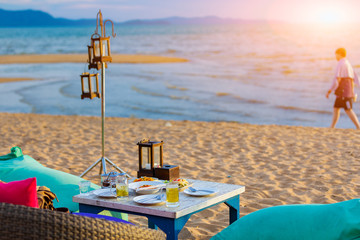 Food and beverage on the table at beach bar for dinning party on the beach and have sunset light and blurry sea background.
