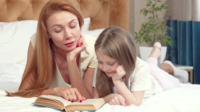 Adorable little girl learning reading at home with her mother. Beautiful woman teaching her little daughter reading. Mom and daughter doing homework. Parenting concept 