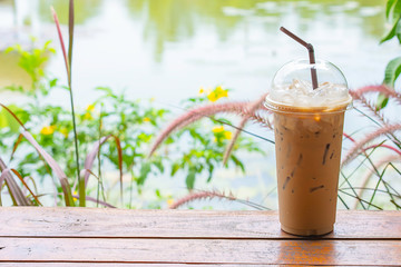 Iced coffee in glass on the table Background  Pennisetum pedicellatum and pond.